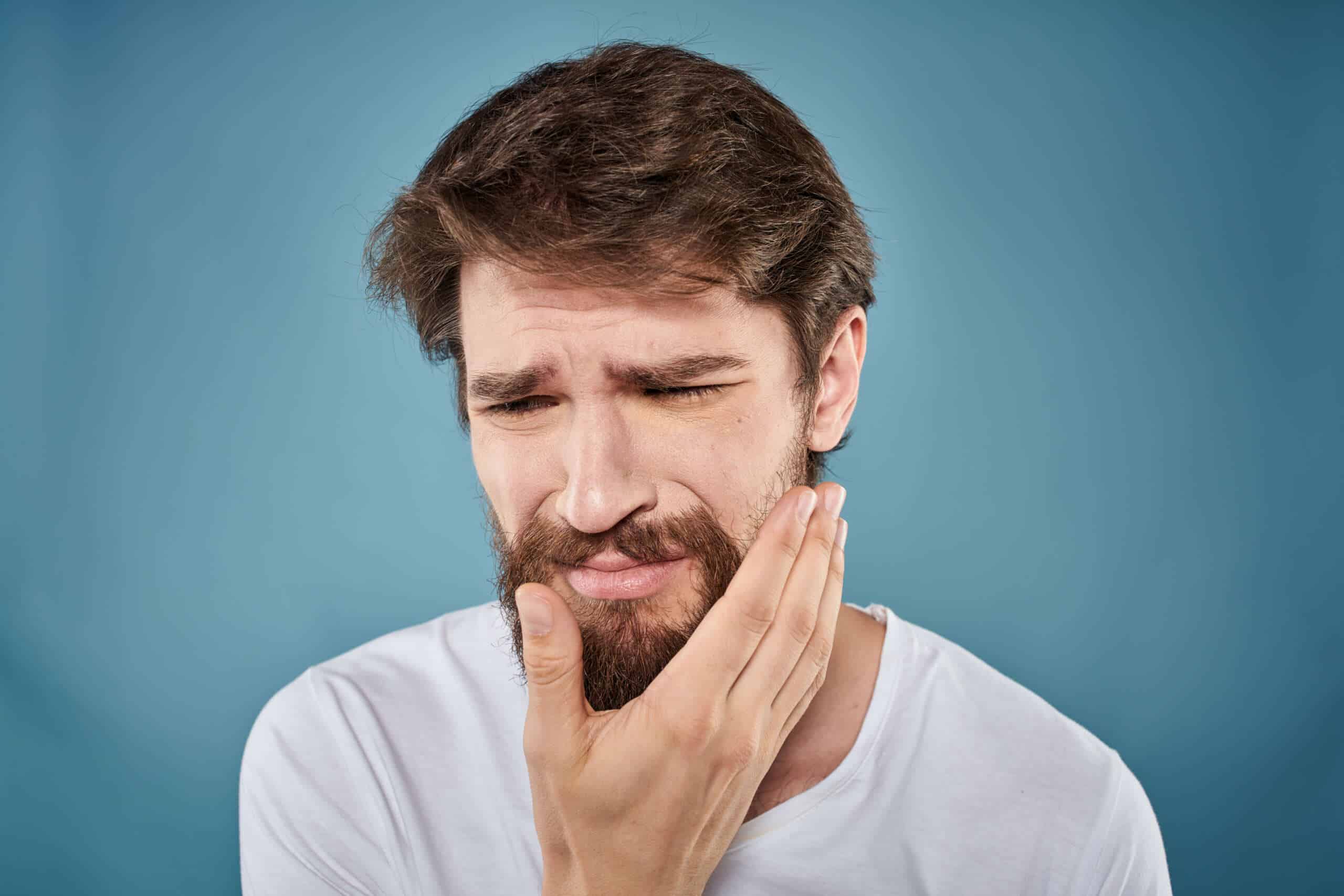 a man holding his cheek as he's suffering from meth mouth sores